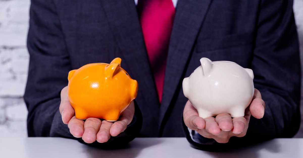 A man in a suit holding an orange and a pink piggy bank, weighing them against each other like loans