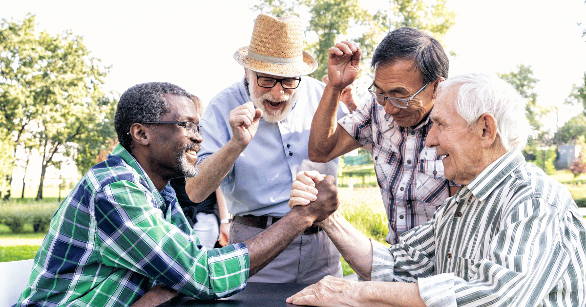 Two pensioners arm wrestling in a park while two other pensioners cheer them on