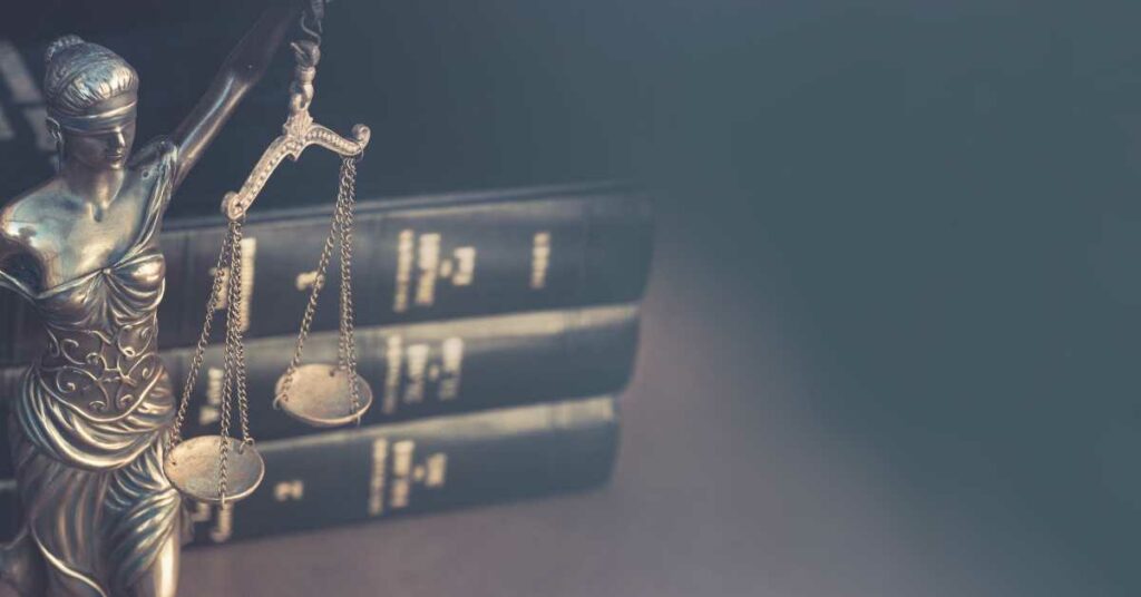 Statue of a blind Lady Justice holding scale in front of lawbooks